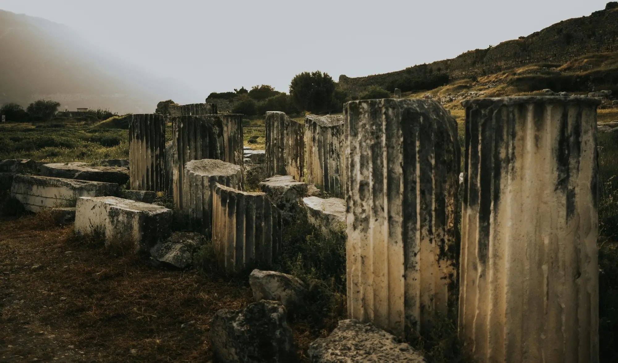 Broken stone column stumps standing in a row at an ancient site, under a grey sky